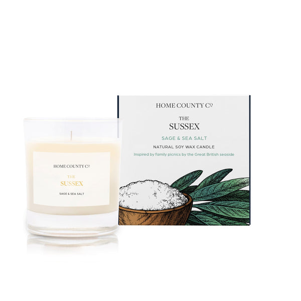 A sage and sea salt scented soy wax candle inspired by Sussex is shown next to its sustainable candle box with sage illustration