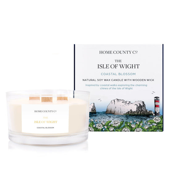 A coastal scented 3 wooden wick soy candle from the Home County Co. is scented with coastal blossom, inspired by the Isle of Wight. The natural candle is shown next to its eco-friendly candle box with a coastline illustration.