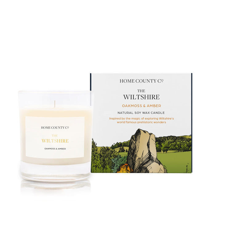 An oakmoss and amber scented soy wax candle inspired by Wiltshire is shown next to its sustainable candle box with stonehenge illustration