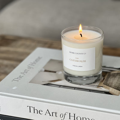 Cotswolds candle from Home County Co is shown lit on a coffee table