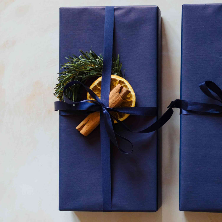 A bluebell scented reed diffuser from the Home County Co. is shown with luxury Christmas Gift Wrap. The reed diffuser is wrapped in luxury navy wrapping paper secured with navy ribbon and Christmas embellishments.