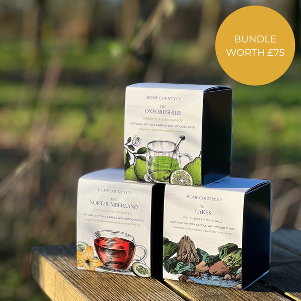 3 county candles in boxes from the Home County Co. are shown stacked in a pyramid outdoors