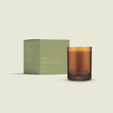 The Orchards candle from the Home County Co. is shown in its amber candle glass vessel next to the luxury gold foiled green box with apple emblem