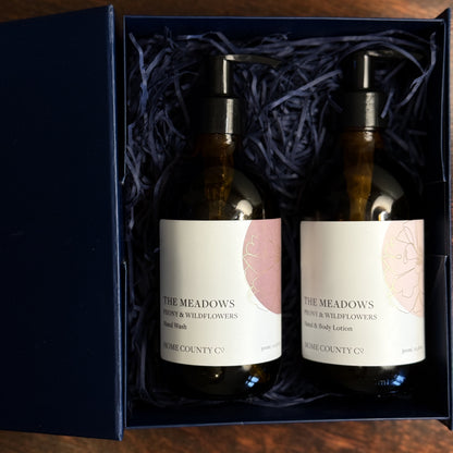The Meadows Peony and Wildflowers liquid hand soap and lotion gift set is shown with the amber bottles in an open gift set box on a table.