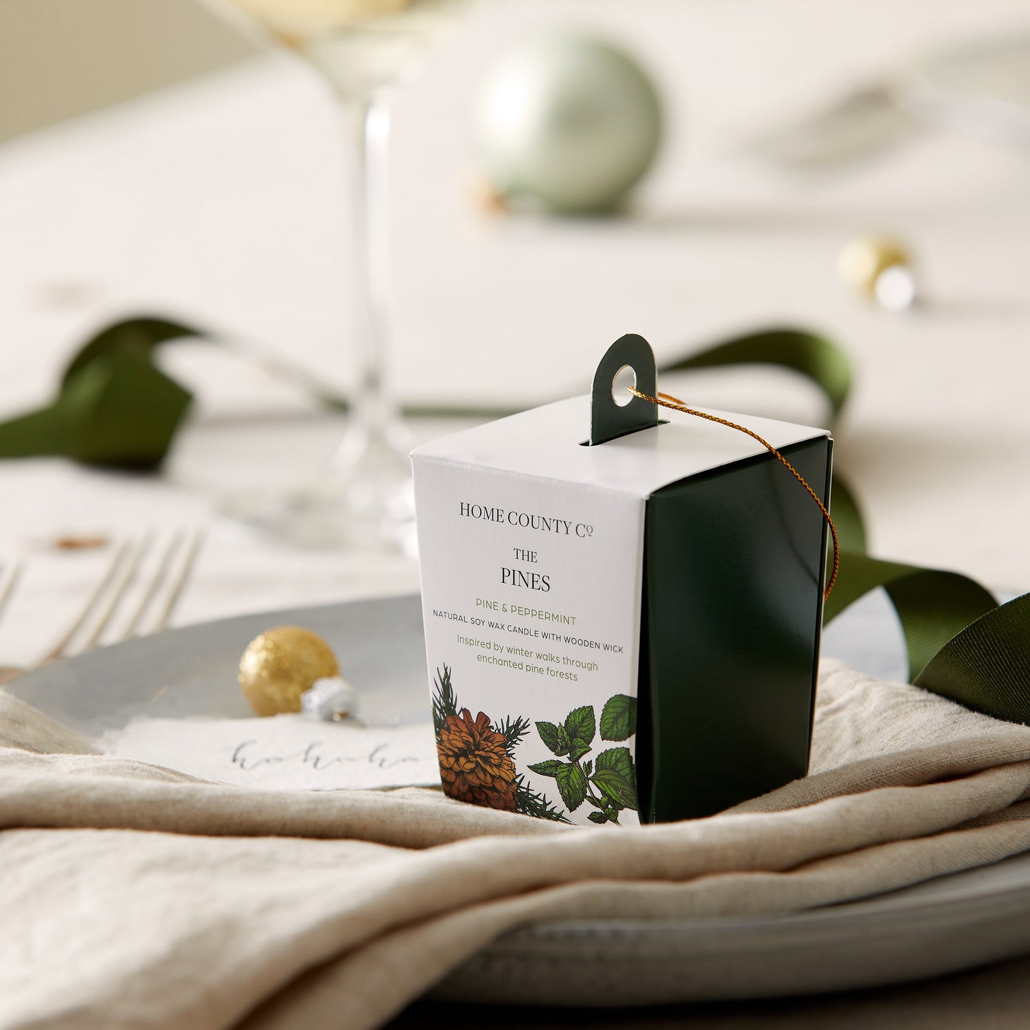 A Pine scented votive Christmas candle from the Home County Co. is shown in eco-friendly packaging on a Christmas table