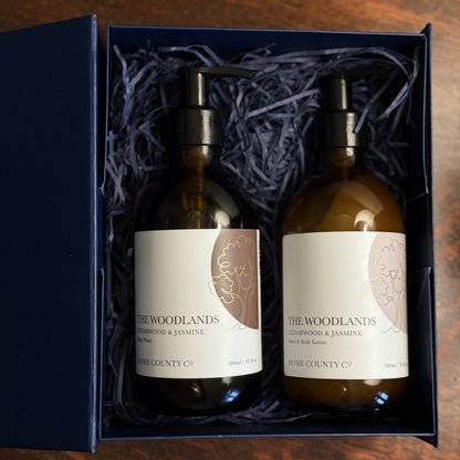 The Woodlands Cedarwood and Jasmine hand soap and lotion gift set is shown open, with the amber glass bottles on a table
