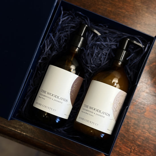 The Woodlands Cedarwood and Jasmine hand soap and lotion gift set is shown open, with the amber glass bottles on a table