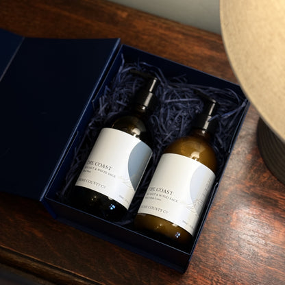 The Coast Sea Salt and Wood Sage scented hand soap and lotion gift set is shown in the open gift box on a table