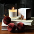 The Mulled Wine scented candle from the Home County Co. is shown alight next to its candle box with Christmas baubles and books in the foreground 