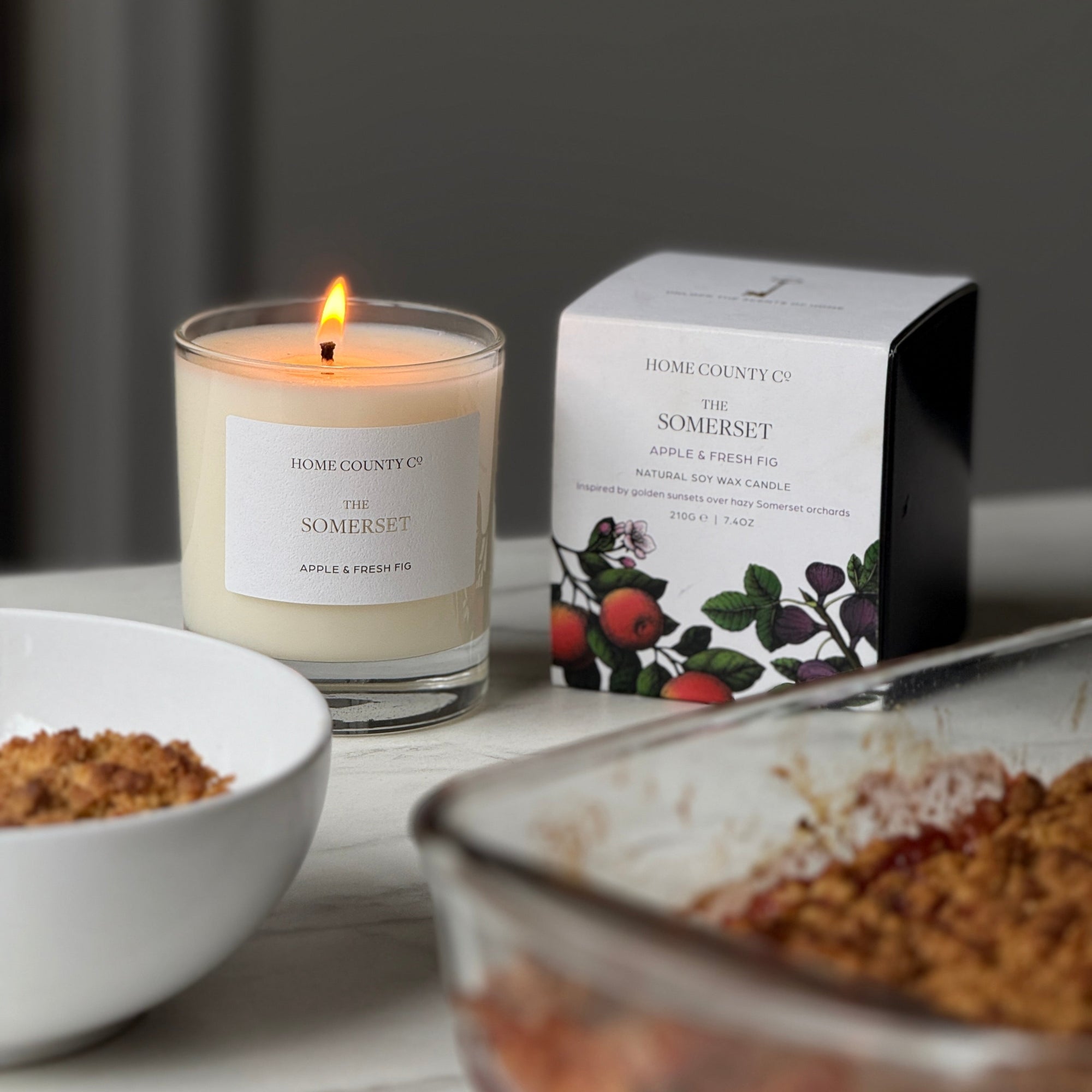 Candle with a lit flame next to a box labeled 'Somerset' on a table.