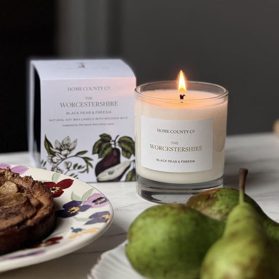 Candle with a Worcestershire label on a table with pears and a plate of food.