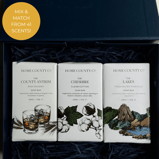 Home County Co. Trio of Soaps gift set shows 3 county-inspired soap bars in a luxury navy gift box with navy shredded paper. Callout says mix and match from 41 scents.