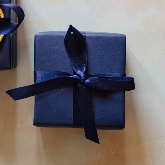 A whiskey scented 200g soy candle from the Home County Co. is shown with luxury Gift Wrap. The candle is wrapped in luxury navy wrapping paper secured with navy ribbon.