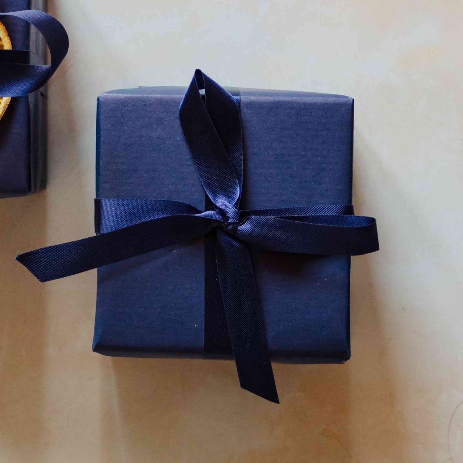 A 200g linen scented soy candle from the Home County Co. is shown with luxury Gift Wrap. The candle is wrapped in luxury navy wrapping paper secured with navy ribbon.