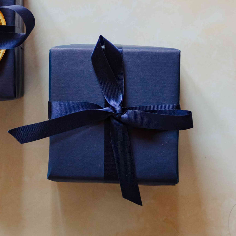 A 200g seaweed scented soy candle from the Home County Co. is shown with luxury Gift Wrap. The candle is wrapped in luxury navy wrapping paper secured with navy ribbon.