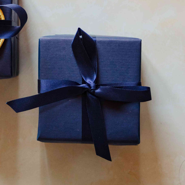 A 200g coastal soy candle from the Home County Co. is shown with luxury Gift Wrap. The candle is wrapped in luxury navy wrapping paper secured with navy ribbon.