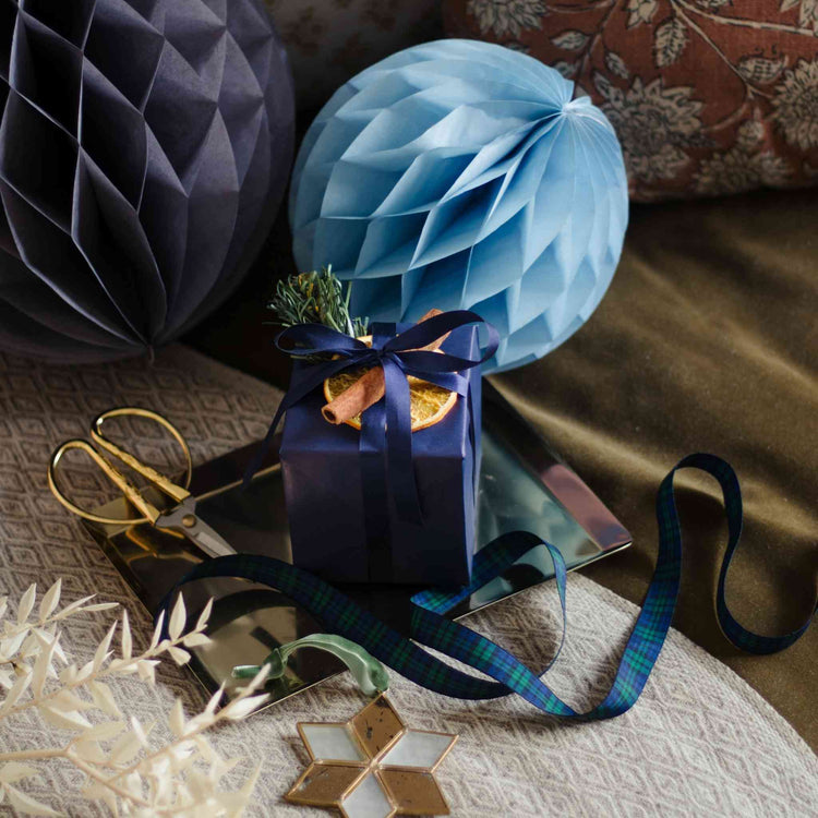 A Home County Co. candle is shown in Christmas gift wrap with navy wrapping paper, a slice of orange and a cinnamon stick