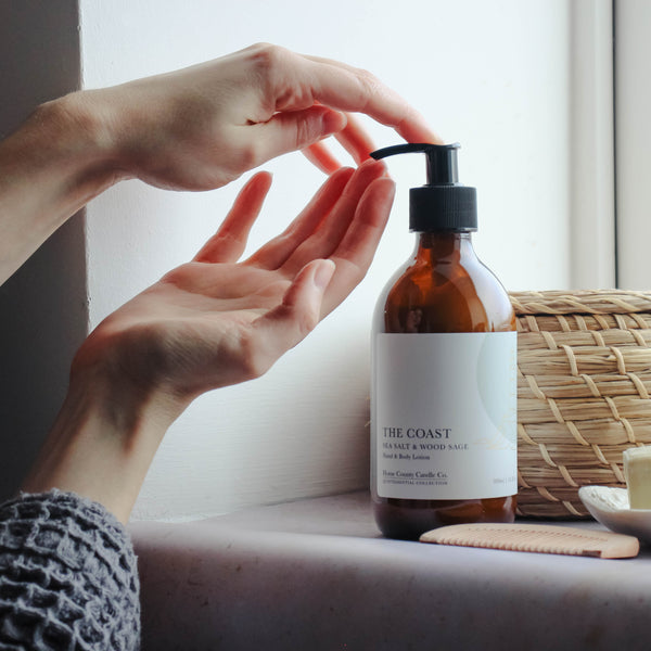 A person applies sea salt and wood sage scented hand and body lotion from the Home County Co. to their hands in a bathroom