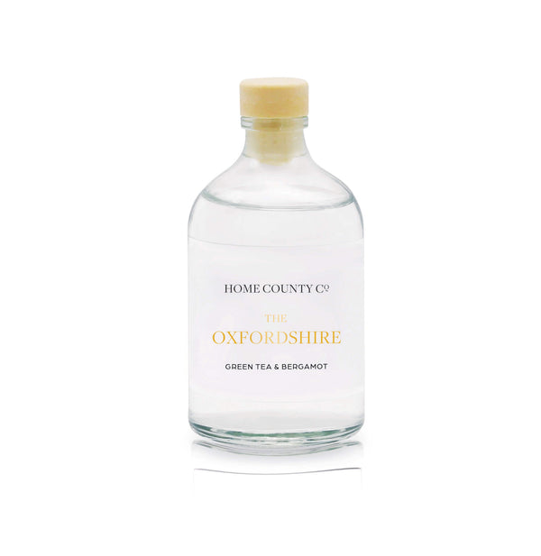 A green tea and bergamot reed diffuser refill is shown in a recyclable glass bottle