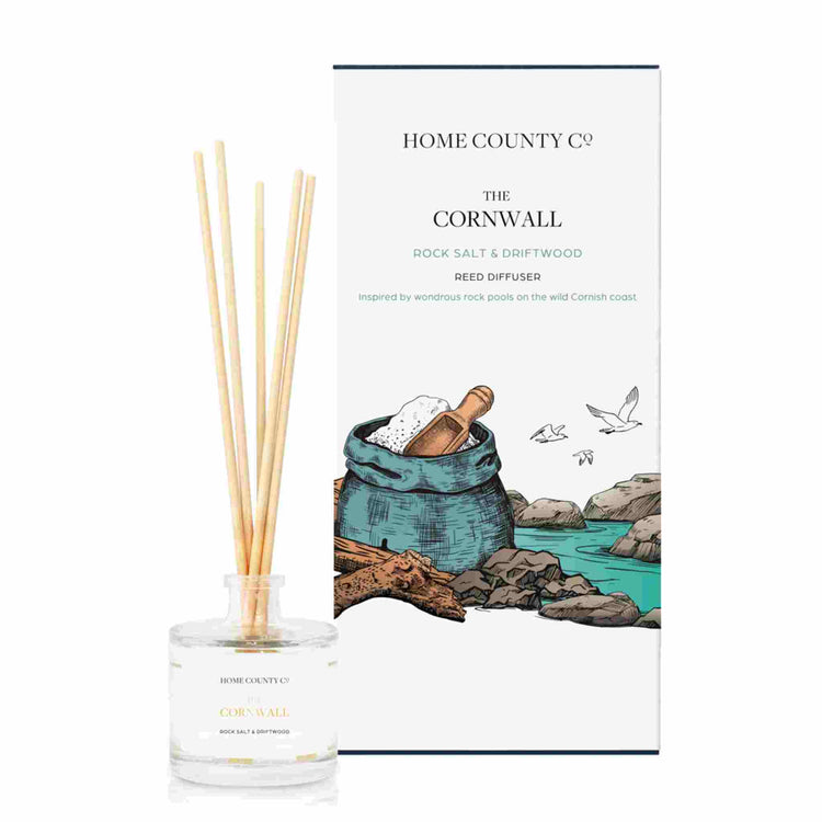 A rock salt and driftwood scented reed diffuser from Home County Co. The vegan friendly reed diffuser is shown next to the eco friendly reed diffuser box packaging.