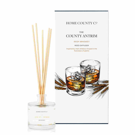 An Irish whiskey scented reed diffuser from Home County Co. The vegan friendly reed diffuser is shown next to the eco friendly reed diffuser box packaging.