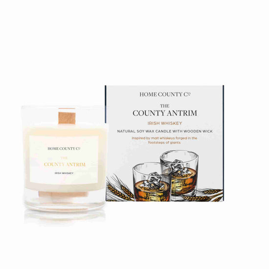 An Irish whiskey scented candle from Home County Co. The wooden wick soy candle is shown next to the eco friendly box packaging.