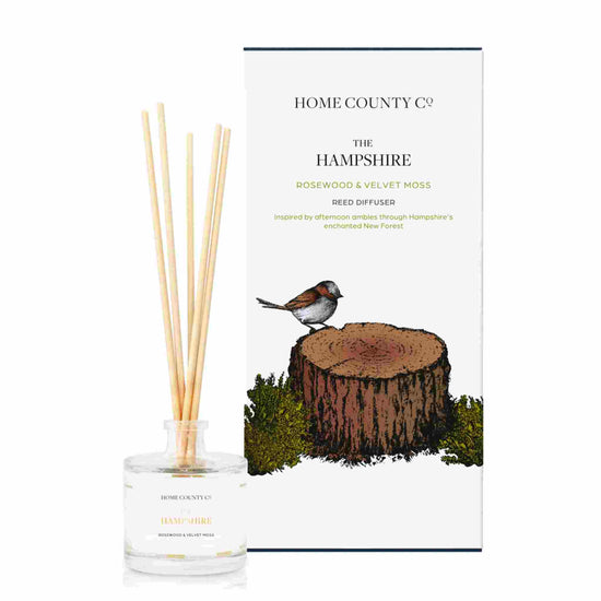 A rosewood and velvet moss scented reed diffuser from Home County Co. The vegan friendly reed diffuser is shown next to the eco friendly reed diffuser box packaging.