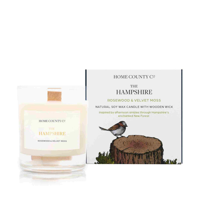 A rosewood and velvet moss scented candle from Home County Co. The wooden wick soy candle is shown next to the eco friendly candle box packaging.