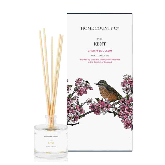 A cherry blossom scented reed diffuser from Home County Co. The vegan friendly reed diffuser is shown next to the eco friendly reed diffuser box packaging.