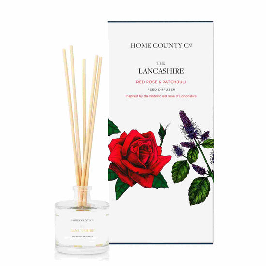 A red rose and patchouli scented reed diffuser from Home County Co. The vegan friendly reed diffuser is shown next to the eco friendly reed diffuser box packaging.