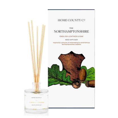 An English leather and oak scented reed diffuser from Home County Co. The vegan friendly reed diffuser is shown next to the eco friendly reed diffuser box packaging.