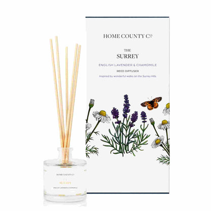 An English lavender and chamomile scented reed diffuser from Home County Co. The vegan friendly reed diffuser is shown next to the eco friendly reed diffuser box packaging.