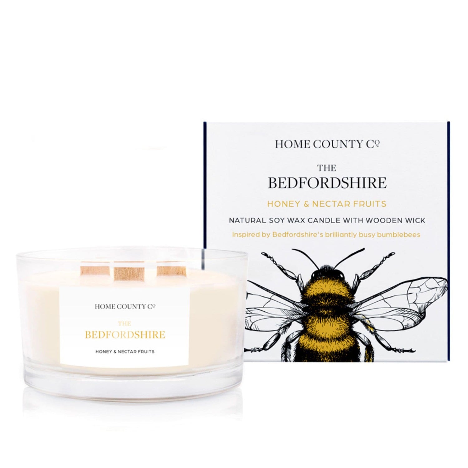 A honey and nectar fruits scented 3 wick candle from the Home County Co. is shown next to its eco-friendly candle packaging box. 