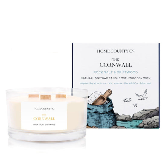 A rock salt and driftwood scented 3 wick candle from the Home County Co. is shown next to its eco-friendly candle packaging box. 