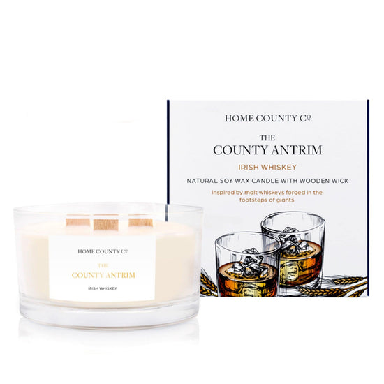 An Irish whiskey scented 3 wick candle from the Home County Co. is shown next to its eco-friendly candle packaging box. 