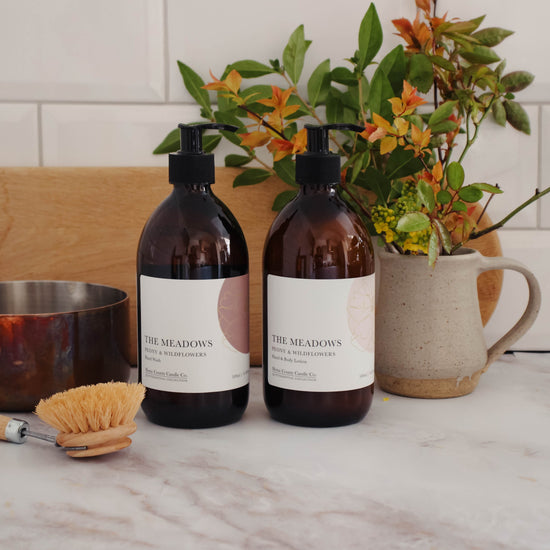 A 500ml floral peony and wildflowers scented hand wash and lotion duo from the Home County Co. is shown in eco-friendly amber glass bottles in a kitchen