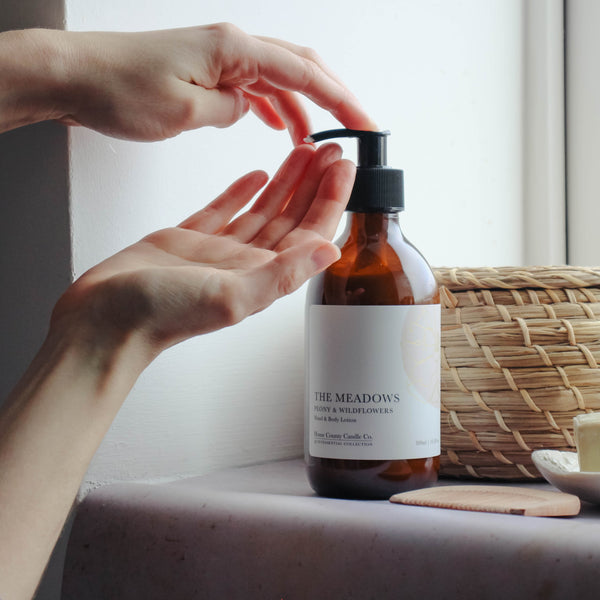 A person applies peony and wildflowers scented hand and body lotion from the Home County Co. to their hands in a bathroom