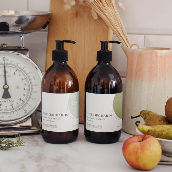 A 500ml fresh fig and green apples scented hand wash and lotion duo from the Home County Co. is shown in eco-friendly amber glass bottles in a kitchen