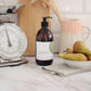 A 500ml fresh fig and apples scented liquid hand wash from the Home County Co. is shown in its eco-friendly amber glass bottle in a kitchen