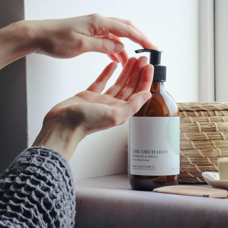 A person is shown pumping 300ml fresh fig and apples scented hand and body lotion from the Home County Co. onto their hands in a bathroom