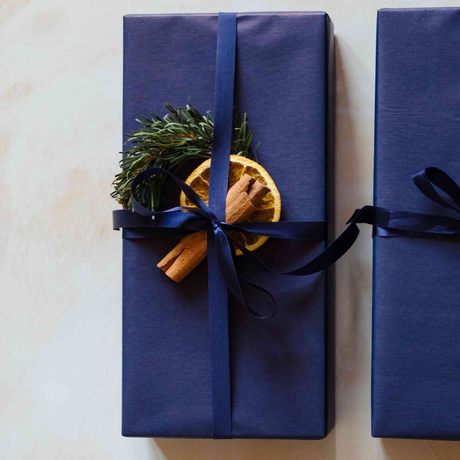 A reed diffuser from the Home County Co. is shown with Christmas Gift Wrap. The reed diffuseris wrapped in luxury navy wrapping paper secured with navy ribbon and embellished with a dried orange slice and a cinnamon stick.