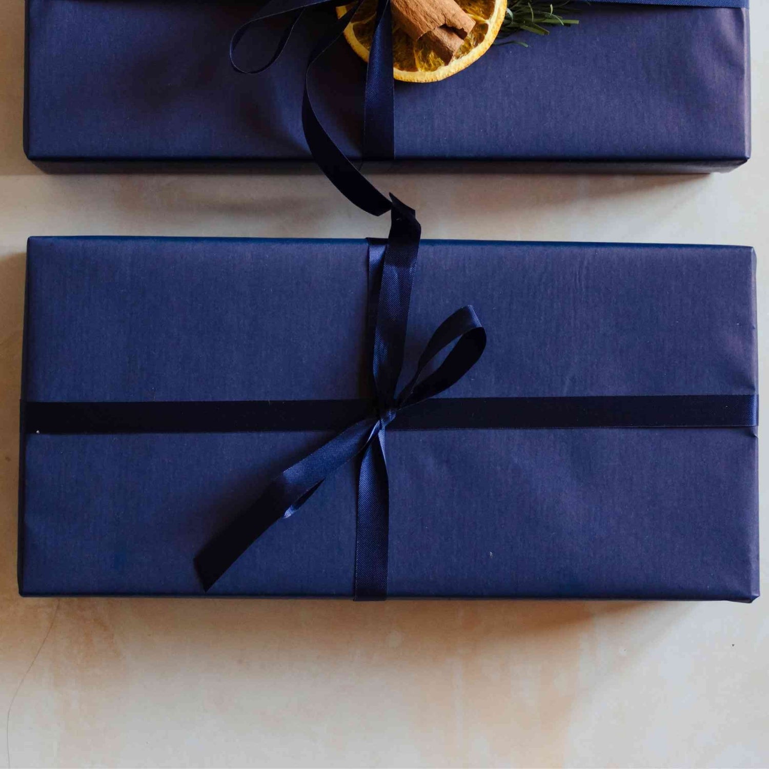 A Christmas candle gift set from the Home County Co. is shown with luxury Gift Wrap. The gift set is wrapped in luxury navy wrapping paper secured with navy ribbon.