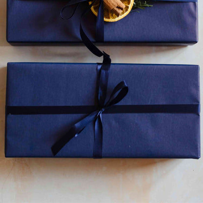 A Christmas candle gift set from the Home County Co. is shown with luxury Gift Wrap. The gift set is wrapped in luxury navy wrapping paper secured with navy ribbon.