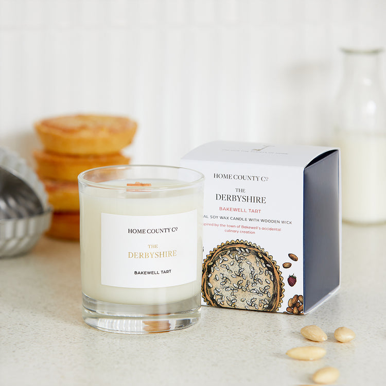 A Derbyshire Bakewell Tart scented candle is shown next to its eco-friendly illustrated candle boc
