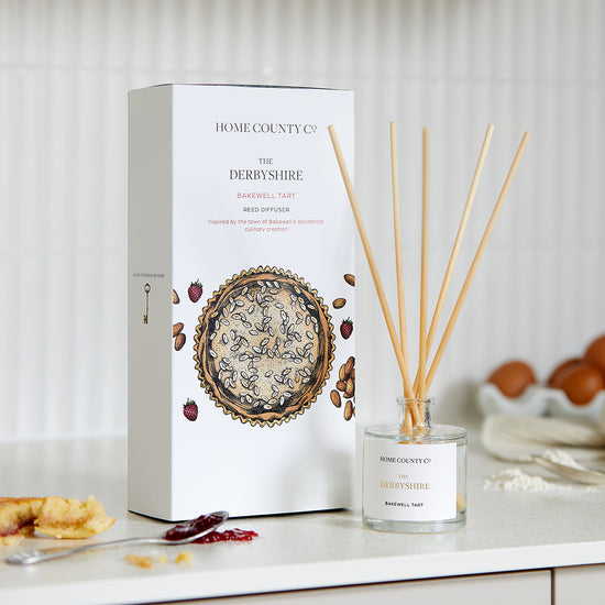 A Derbyshire Bakewell Tart scented reed diffuser is shown next to its eco-friendly illustrated reed diffuser box