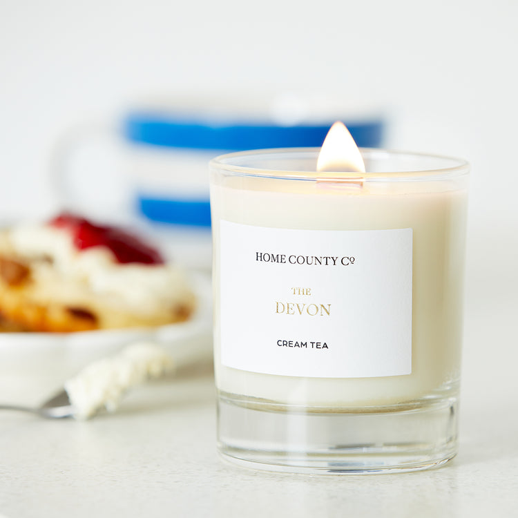 A Devon cream tea scented candle from the Home County Co. is shown alight next to a cream tea