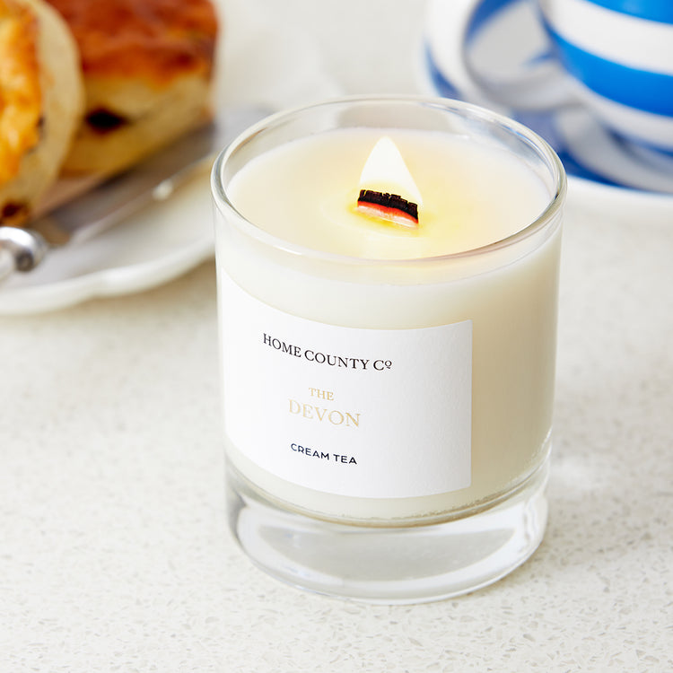 A Devon cream tea scented candle from the Home County Co. is shown alight next to a cream tea 