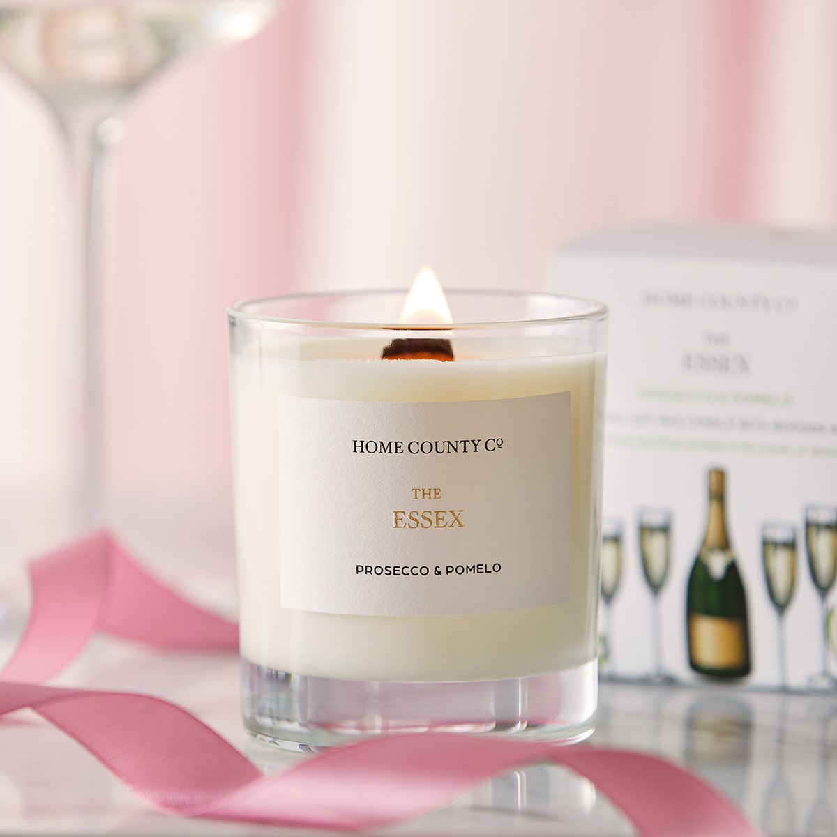 A Prosecco and Pomelo scented candle from the Home County Co is shown alight next to the illustrated candle packaging