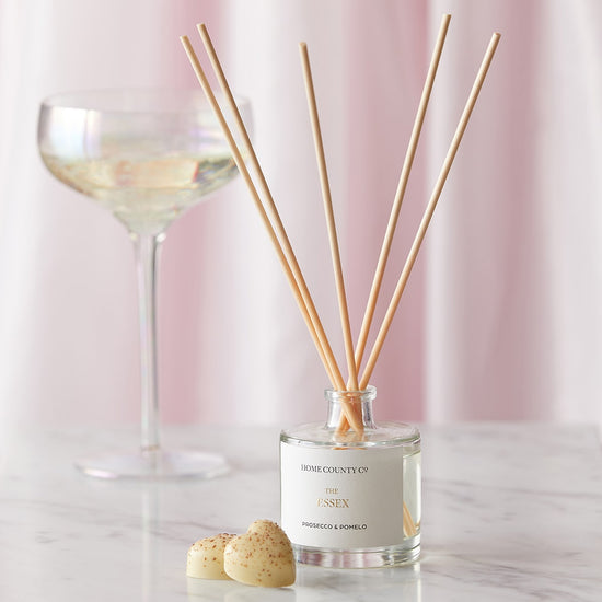 An Essex prosecco and pomelo scented reed diffuser from the Home County Co. is shown in use next to a glass of prosecco