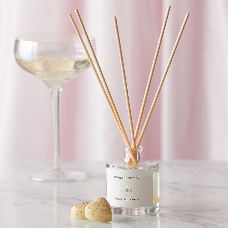 An Essex prosecco and pomelo scented reed diffuser from the Home County Co. is shown in use next to a glass of prosecco